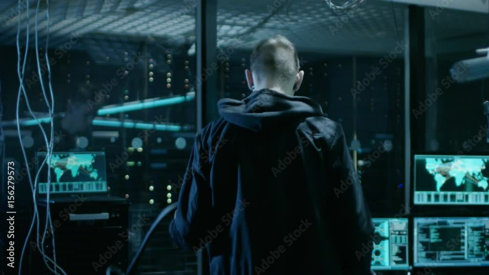 Poster hooded hacker takes his place in at his desk in hacker's lair. place is neon, dark and has many disp
