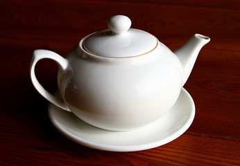 White teapot and the saucer on the wooden table alone close up
