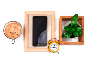 Cell phone with black blank screen and green plant in wooden frames with cup of coffee and yellow alarm clock