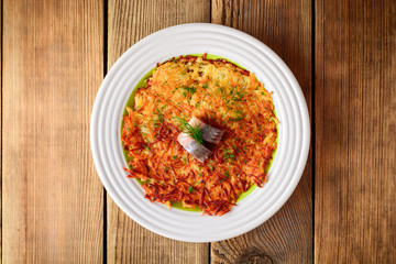 Potato rosti with dill and salted herring in plate on wooden table.