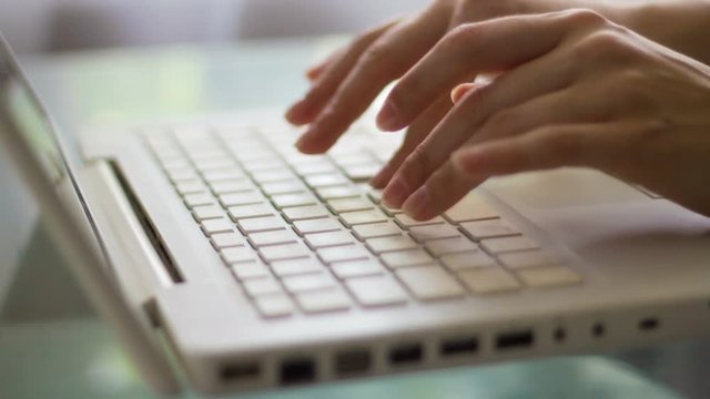 Close-up of a woman typing on a laptop keyboard
