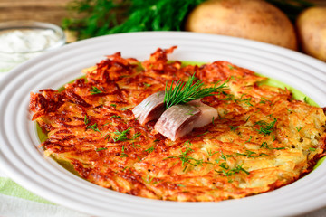 Potato rosti with dill and salted herring in plate on wooden table.