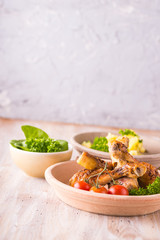 Portion of chicken legs on plate in front of  potatoes and salad
