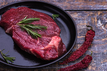 Raw Beef Steak, salt, pepper, garlic, rosemary  on the black pan, wooden board, background.