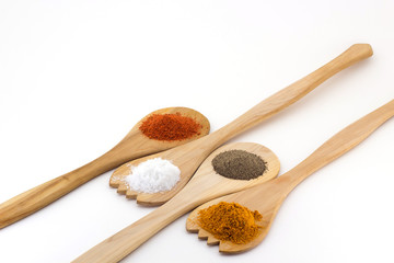Spices on three wooden spoons isolated on white background