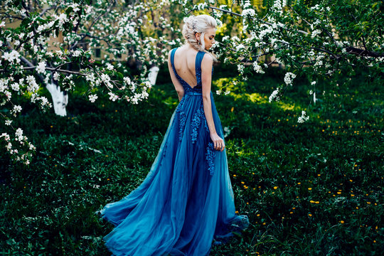 Beautiful young girl in a long evening blue dress in an apple blossoming garden