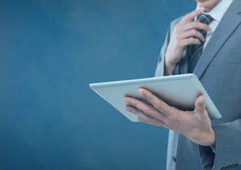 Businessman holding tablet against blue foggy background