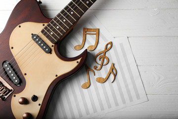 Musical notes, sheet and guitar on white wooden background, closeup