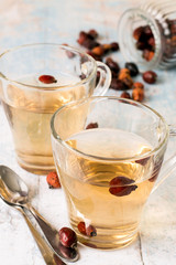  Freshly prepared infusion of dry fruit rose hips in glass transparent mug on a light wooden background.