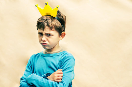 Angry boy with a crown on his head on a light background