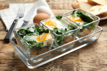 Delicious eggs Florentine in glass baking dishes on wooden table