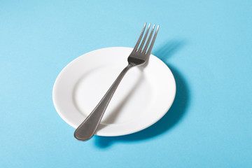 White empty plate with fork on blue tablecloth
