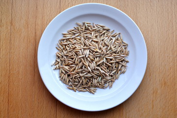 handful of oat grains on white plate on wooden table