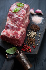 Close-up of raw seasoned pork neck meat on a black wooden background, selective focus, studio shot