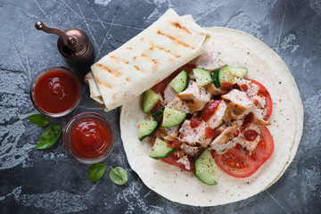 Shawarma with roasted chicken meat and vegetables over grey stone background, top view