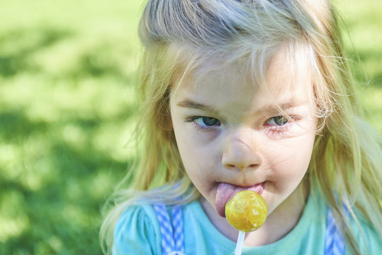 Happy little child blond girl with lollipop resting on the grass in summer day