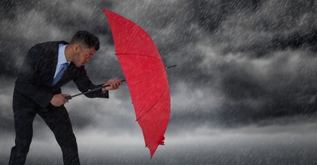 Business man blocking rain with umbrella against storm clouds