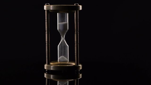 Time Lapse of Sand Flowing Through vintage metal hourglass on black background.