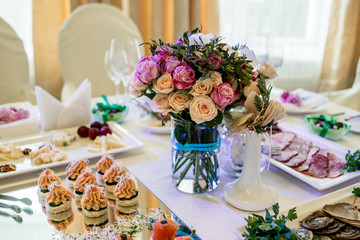 Beautiful wedding bouquet of cream and pink roses in glass vase on dinner table, selective focus. Table setting at a luxury wedding reception. Flowers on the table