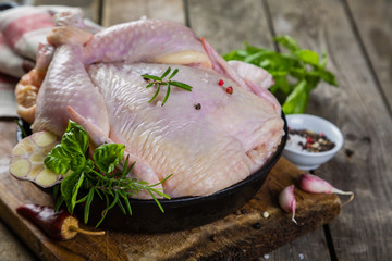 Raw whole chicken with herbs and spices on rustic wood background