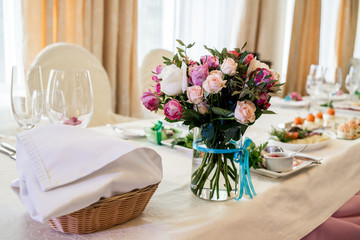 Beautiful wedding bouquet of cream and pink roses in glass vase on dinner table, selective focus. Table setting at a luxury wedding reception. Flowers on the table