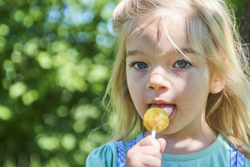 Happy little child blond girl with lollipop resting on the grass in summer day © Petr Bonek