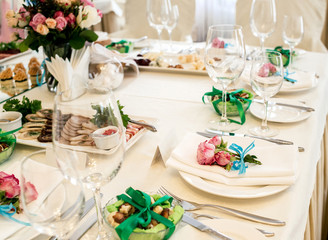 Pink roses with blue ribbon on white empty plate with white napkin on dinner table. Table setting. Table served for wedding banquet, close up view