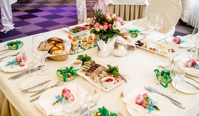 Beautiful wedding bouquet of cream and pink roses in glass vase on dinner table in blur, selective focus. Table setting at a luxury wedding reception. Flowers on the table