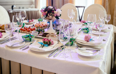 Pink roses with blue ribbon on white empty plate with white napkin on dinner table in blur. Table setting. Table served for wedding banquet, close up view
