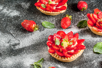 Summer and spring dessert. Home pies tartlets with custard and strawberries, decorated with mint and powdered sugar. On black stone table. Copy space