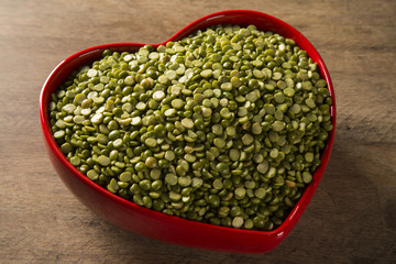 Green lentils inside a heart pot on wood background. Edible raw pulses of the legume family.