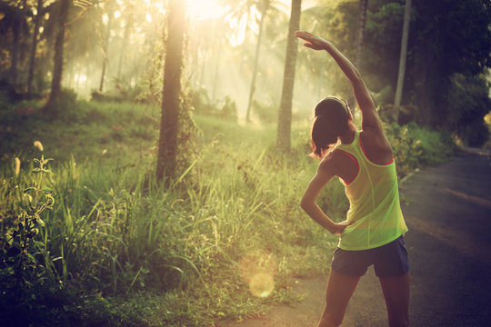 Young Female Runner Warming Up Before Running At Morning Forest Trail