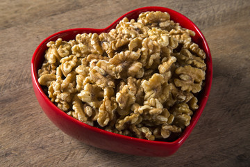 walnuts in heart bowl on wood table.