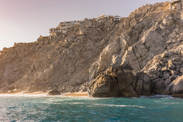 Resort vacation houses and villas nested in the rock formations around the Arch in Cabo San Lucas, Mexico at sunset. Interesting shapes of cliffs and stones, beautiful blue water and sunlight.