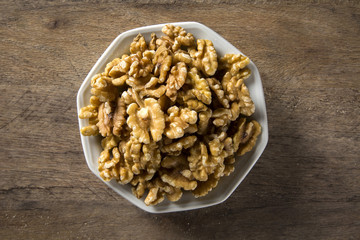 walnuts in white bowl on wood table.