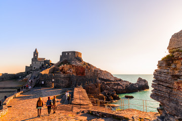 A scenic view of the cathedral of Porto Venere at sunset with people walk and admire the view.