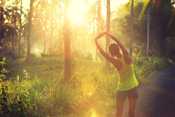 Young female runner stretching arms before running at morning forest trail