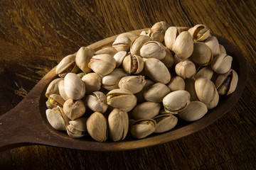 pistachio nuts in wood spoon on wood background
