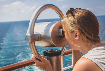 Junge Frau schaut durch ein Fernglas auf einem Kreuzfahrtschiff