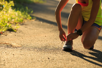 Young fitness woman runner tying shoelace on morning tropical forest trail
