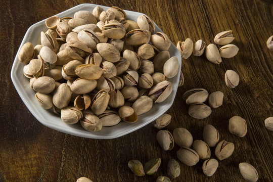 pistachio nuts in white bowl with wood background.