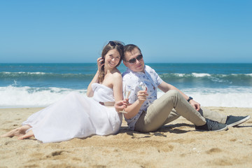 Fototapeta na wymiar Young romantic couple sitting on the beach drinking champaign