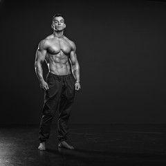 Fototapeta na wymiar Black and white photo of Muscular and fit young fitness model posing over black background.