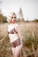 Fototapeta na wymiar Beautiful and elegant smiling sexy blonde woman with red lips and hair waves wearing beige liingerie posing on the field outdoors summer, retro vintage style and fashion. 