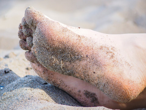 Feet of one unrecognizable caucasian person resting in sand, with wet sand on foot soles