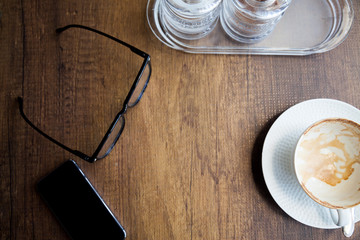 work space in coffee shop on table have phone, glasses, coffee cup and two jar of sugar on top view.