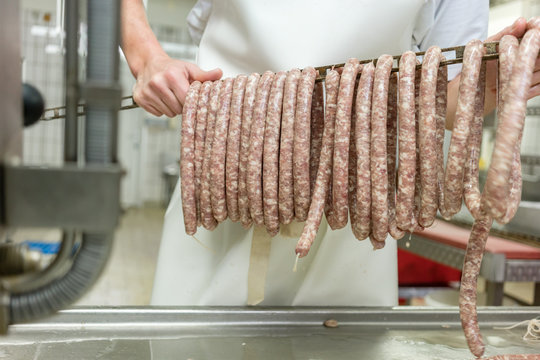 Butcher putting sausages on beam in butchery
