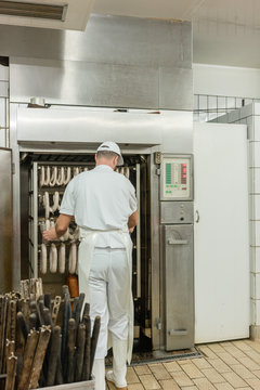 Butcher preparing sausages and meat for curing in smoking room