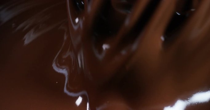 Delicious brown chocolate is prevented by a machine at a professional factory making sweets, on a chocolate background. Concept: the production of sweetness, cream, chocolate, delicious air, gourmet.