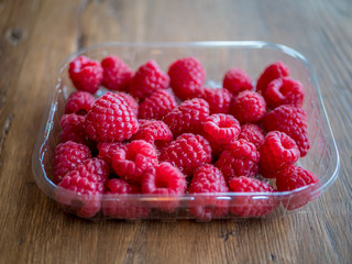 Fresh raspberry in plastic box on wooden table.